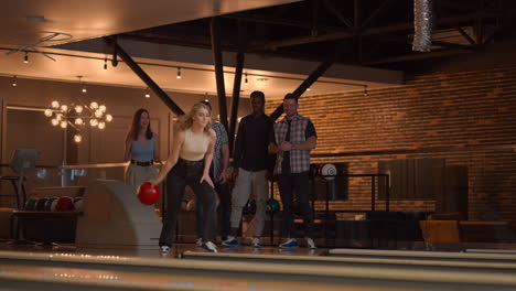 A-beautiful-blonde-throws-a-bowling-ball-and-knocks-out-a-shot-with-one-throw-and-hugs-and-rejoices-with-her-friends.-Multi-ethnic-group-of-friends-bowling