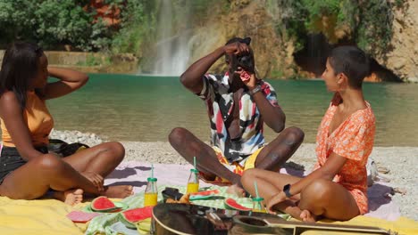 Black-man-taking-photo-of-women-sitting-on-beach