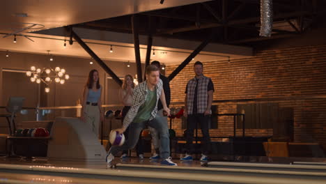 A-Caucasian-man-throws-a-bowling-ball-and-knocks-out-a-shot-with-one-throw-and-hugs-and-rejoices-with-his-friends.-Multi-ethnic-group-of-friends-bowling