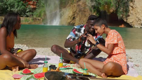 Black-man-taking-photo-of-women-sitting-on-beach