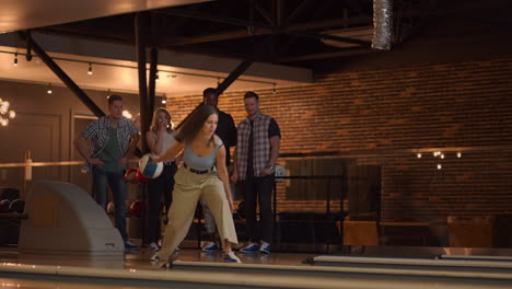 A-Caucasian-brunette-woman-throws-a-bowling-ball-and-knocks-out-a-shot-with-one-throw-and-hugs-and-rejoices-with-her-friends.-Multi-ethnic-group-of-friends-bowling