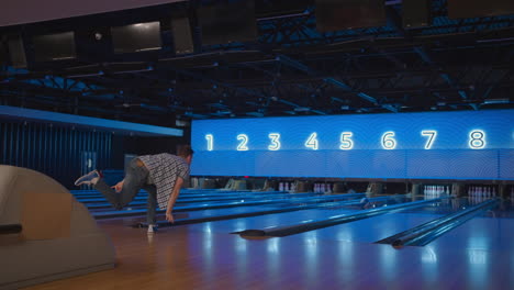 A-young-man-in-a-bowling-alley-throws-a-ball-in-slow-motion-and-knocks-down-skittles.-Play-bowling.-Throw-balls-on-the-floor-of-the-bowling-club