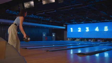 A-brunette-woman-in-bowling-throws-a-ball-in-slow-motion-and-knocks-down-skittles.-Play-bowling.-Throw-balls-on-the-floor-of-the-bowling-club