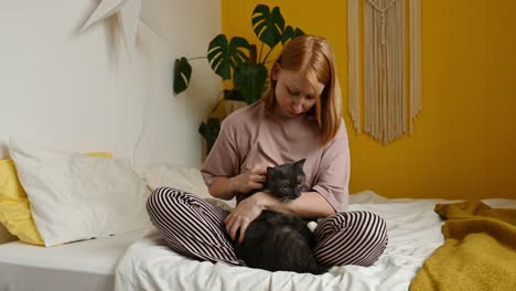 Smiling-woman-embracing-fluffy-cat-in-bedroom