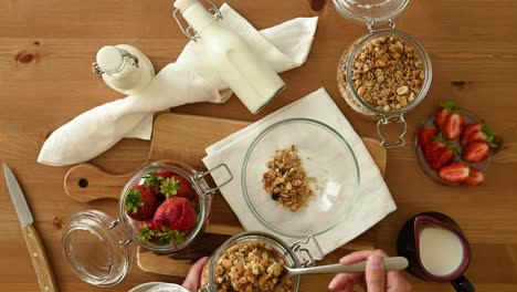 Crop-person-preparing-breakfast-with-granola-milk-and-strawberries