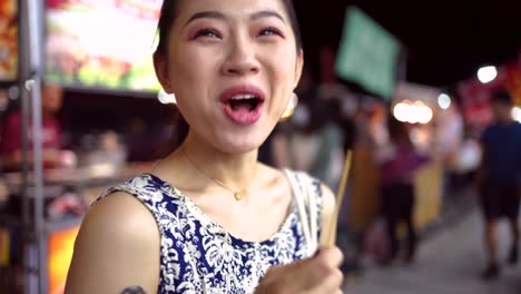 Cheerful-Asian-woman-eating-potato-balls-on-street