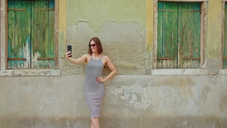 Cheerful-female-traveler-taking-selfie-near-shabby-wall