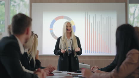joyful-blonde-woman-is-speaking-in-business-meeting-standing-against-charts-female-expert