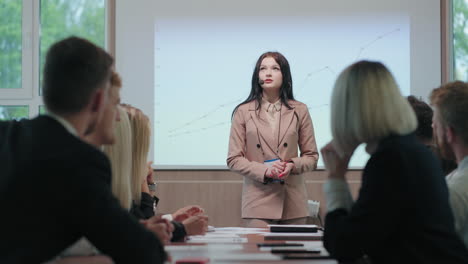 young-businesswoman-is-speaking-in-conference-hall-in-front-of-colleagues-and-partners