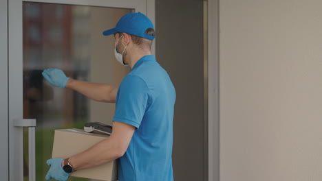 A-delivery-man-wearing-a-protective-mask-and-gloves-passes-the-parcel-to-the-customer-and-receives-a-contactless-payment-via-NFC