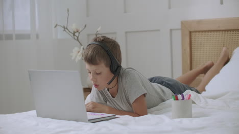 Ein-Kleiner-Junge-Nutzt-Einen-Modernen-Laptop-Mit-Webcam-Und-Drahtlosen-Kopfhörern,-Um-Mit-Freunden-Zu-Kommunizieren,-Die-Zu-Hause-Bleiben