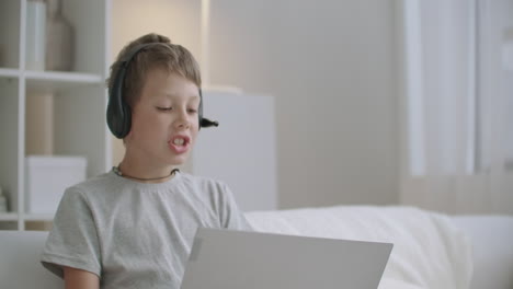 Der-Kleine-Junge-Sitzt-Zu-Hause-Auf-Dem-Bett-Und-Chattet-Online-Per-Notebook-Und-Spricht-über-Das-Mikrofon-Von-Kopfhörern