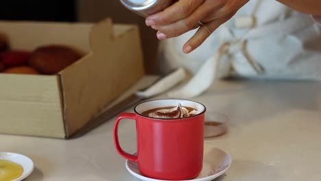 Crop-barista-adding-cinnamon-in-cup-with-cocoa-drink