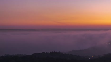 Luftaufnahme-Der-Modernen-Stadt-Und-Der-Mit-Zeckenwolken-Bedeckten-Berge-Unter-Buntem-Himmel-Bei-Sonnenuntergang