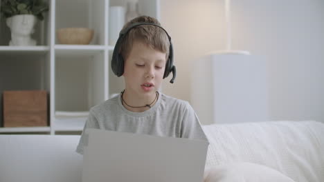 Internetsüchtiger-Kleiner-Junge-Nutzt-Laptop-Zum-Kommunizieren-Und-Spielen,-Sitzt-Auf-Dem-Bett-Und-Zeichnet-Auf-Papier
