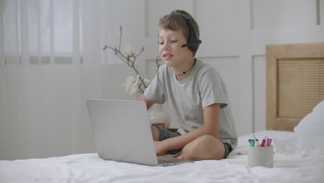 Retrato-De-Un-Niño-Pequeño-Mirando-La-Pantalla-De-Una-Computadora-Portátil-Y-Dibujando-En-Un-Cuaderno-Escuchando-Música-Con-Auriculares