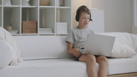 little-boy-is-talking-to-someone-by-online-video-call-using-notebook-with-internet-and-headphones-staying-home-at-vacation