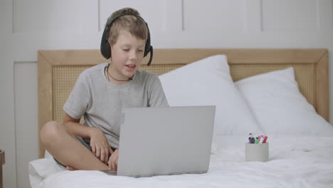 Der-Kleine-Junge-Zeichnet,-Liegt-Auf-Dem-Bett-In-Seinem-Zimmer-Und-Kommuniziert-Online-Per-Webcam-Und-Kopfhörer