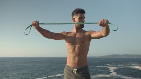 Determined-athletic-man-training-with-elastic-band-near-sea