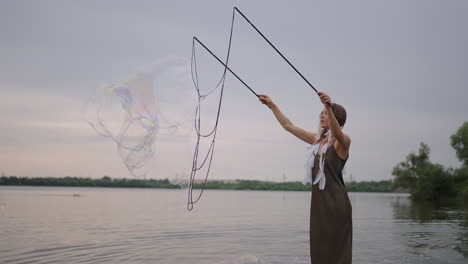 A-young-girl-artist-shows-magic-tricks-using-huge-soap-bubbles.-Create-soap-bubbles-using-sticks-and-rope-at-sunset-to-show-a-theatrical-circus-show
