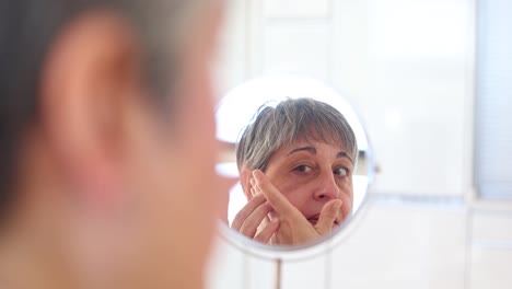 Elderly-woman-in-bathrobe-applying-facial-cream