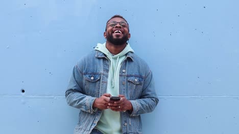 Cheerful-black-man-browsing-smartphone-near-wall