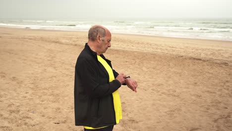 Aged-sportsman-checking-smart-watch-on-beach