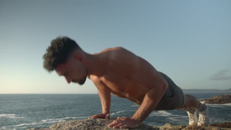 Man-with-naked-torso-doing-push-ups-exercises-on-rocky-shore