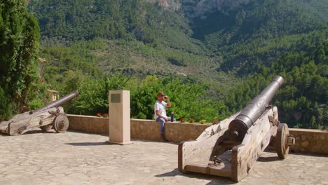 Male-traveler-resting-and-drinking-coffee-on-ancient-cannon
