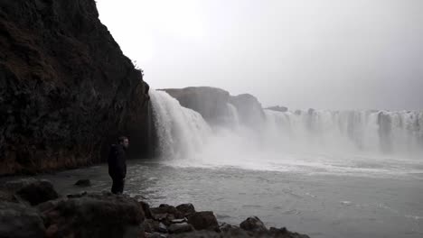 Tourist-standing-on-stone-near-foamy-waterfall