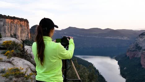 Young-woman-photographing-mountains-on-camera-placed-on-tripod