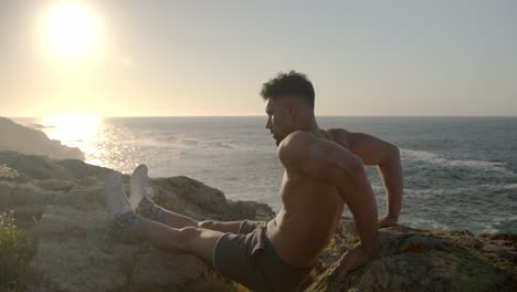 Man-with-naked-torso-doing-triceps-exercises-on-rocky-shore