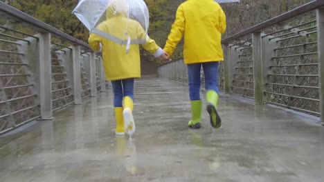 Kids-in-rubber-boots-walking-on-bridge-during-rain
