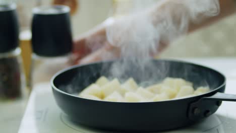Woman-adding-salt-to-frying-potatoes-in-pan