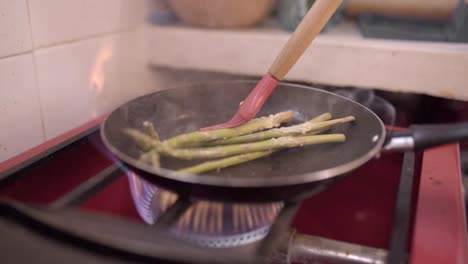 Unrecognizable-chef-frying-asparagus-in-kitchen