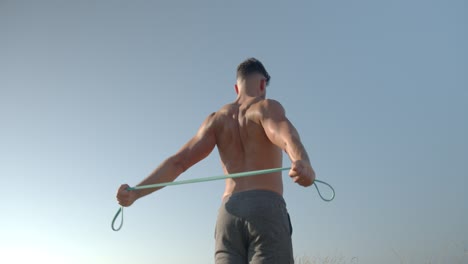 Determined-athletic-man-training-with-elastic-band-near-sea