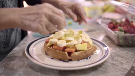 Woman-preparing-sweet-waffles-with-fruits-for-breakfast