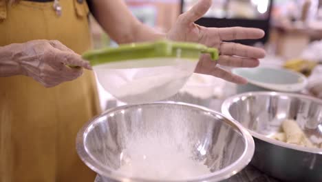 Mature-woman-sifting-flour-in-metal-bowl-in-kitchen