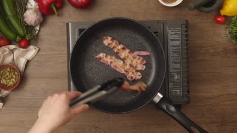 Unrecognizable-cook-frying-bacon-in-pan
