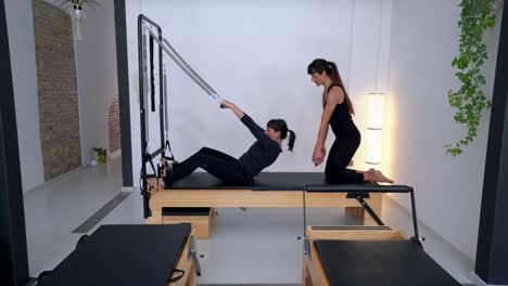 Frau-Macht-Übungen-Auf-Dem-Pilates-Reformer-Mit-Trainer