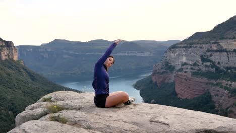 Young-Hispanic-sportswoman-stretching-body-during-training-in-rocky-mountains