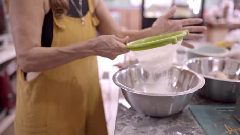 Mature-woman-sifting-flour-in-metal-bowl-in-kitchen