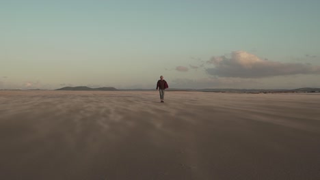 Man-walking-on-sandy-beach-at-sundown