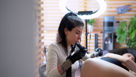 Tattooer-drawing-tattoo-on-hip-of-client-in-studio