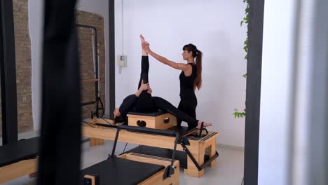 Woman-stretching-legs-on-pilates-reformer-with-help-of-personal-coach