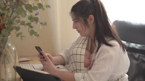 Mother-with-newborn-baby-chatting-on-smartphone-at-home