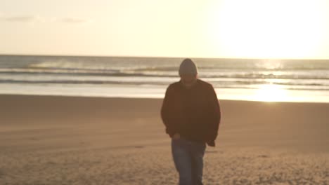 Man-walking-on-sandy-beach-at-sundown