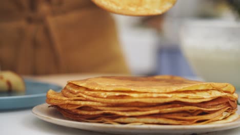 Anonymous-cook-taking-a-pancake-from-a-plate-with-several-pancakes-on-it