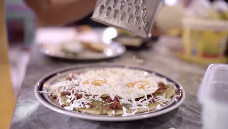 Unrecognizable-person-grating-cheese-on-meal-with-eggs-and-nachos
