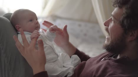 Crop-father-playing-and-talking-to-newborn-baby-at-home